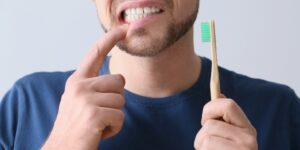 Man pointing to bleeding gums while holding a toothbrush – 92 Dentistry, Portland, OR