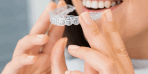 Person holding and smiling with a clear Invisalign aligner.