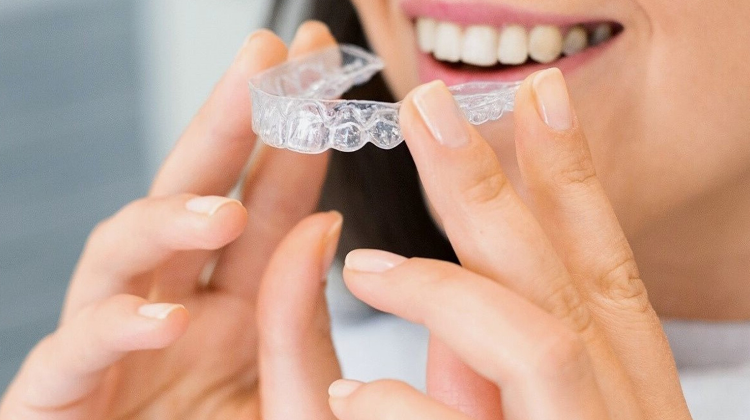 Person holding and smiling with a clear Invisalign aligner.