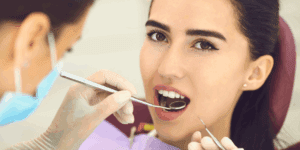 Woman receiving dental checkup with mirror and scaler at dentist.