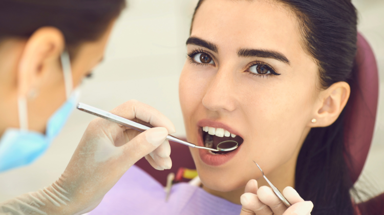 Woman receiving dental checkup with mirror and scaler at dentist.